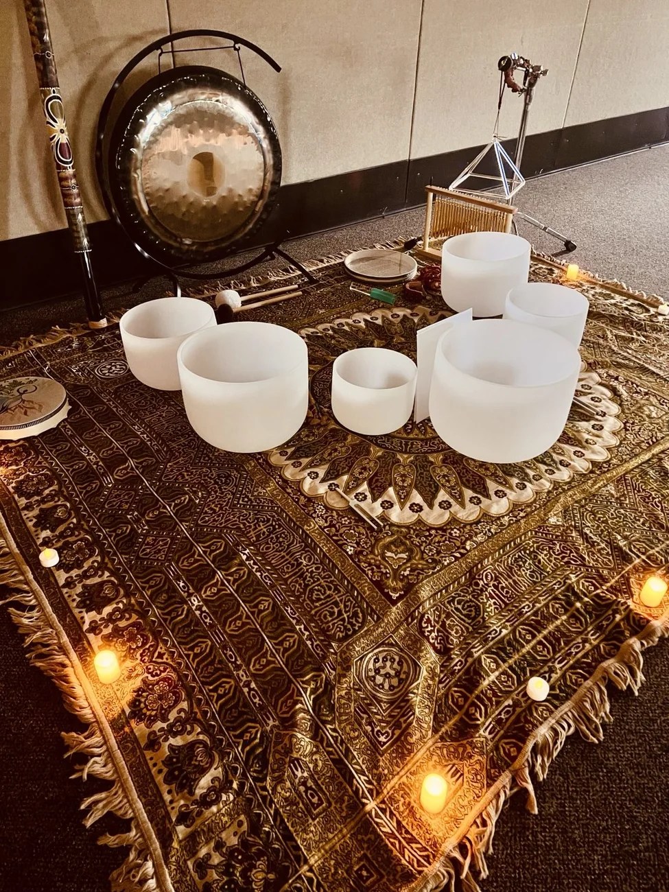 Crystal singing bowls and gong arranged on a patterned cloth with warm lights