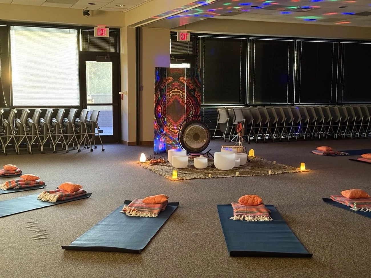 Mats arranged facing a gong and singing bowls beneath soft colored light